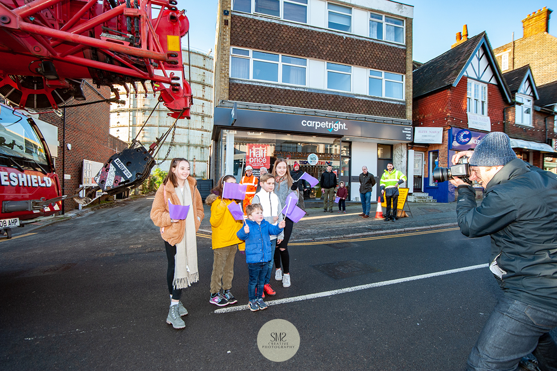 Local children pose for photographs waving purple Oxted Regen flags to witness the arrival of the crane. 