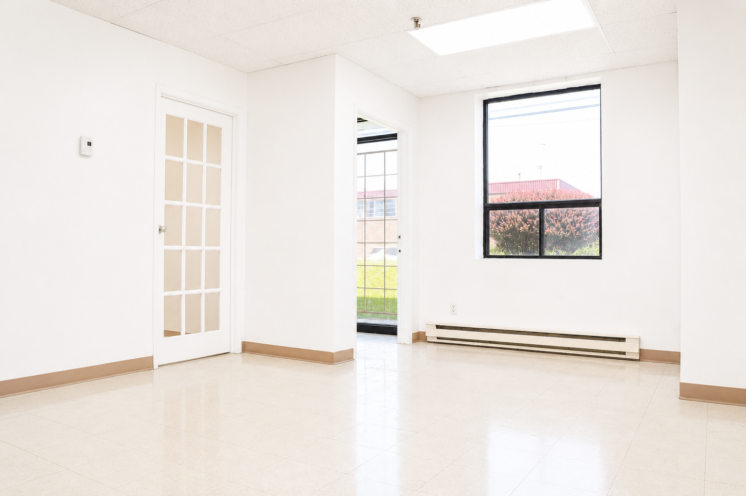 Empty room with white walls, a door with glass panels, a large window, and a heater along the base of the wall.