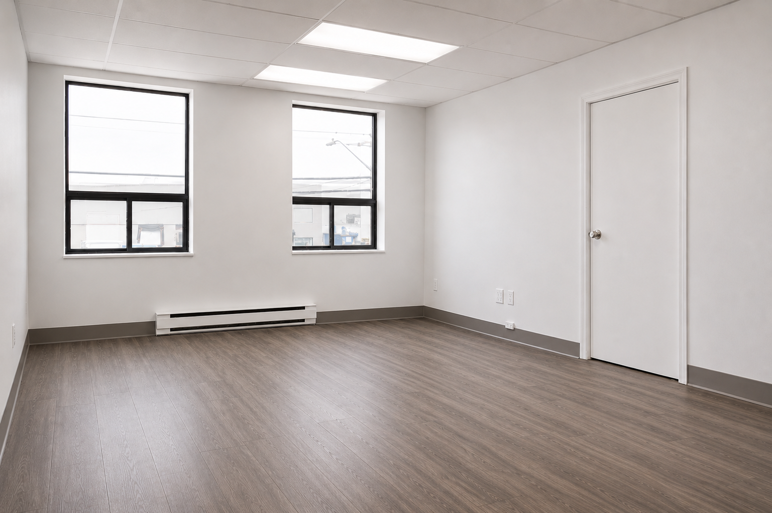 Empty room with white walls, wood floor, two windows, and a closed door.
