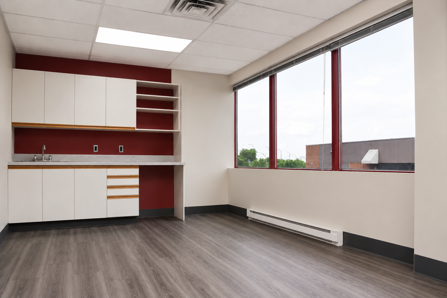 Empty kitchen with white cabinets, brown drawers, red accent wall, large windows, and gray flooring.