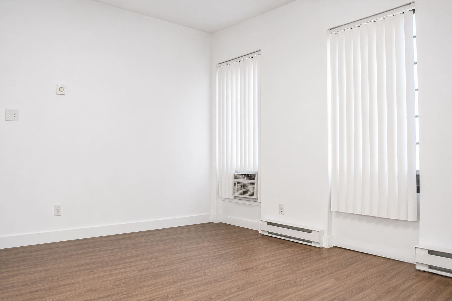 Empty room with wooden floor, white walls, two large windows with vertical blinds, and an air conditioning unit in one window.