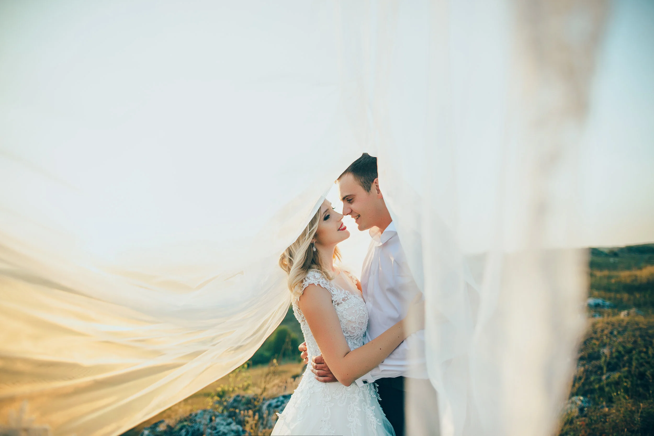 wedding couple covered with bridal vail at sunset