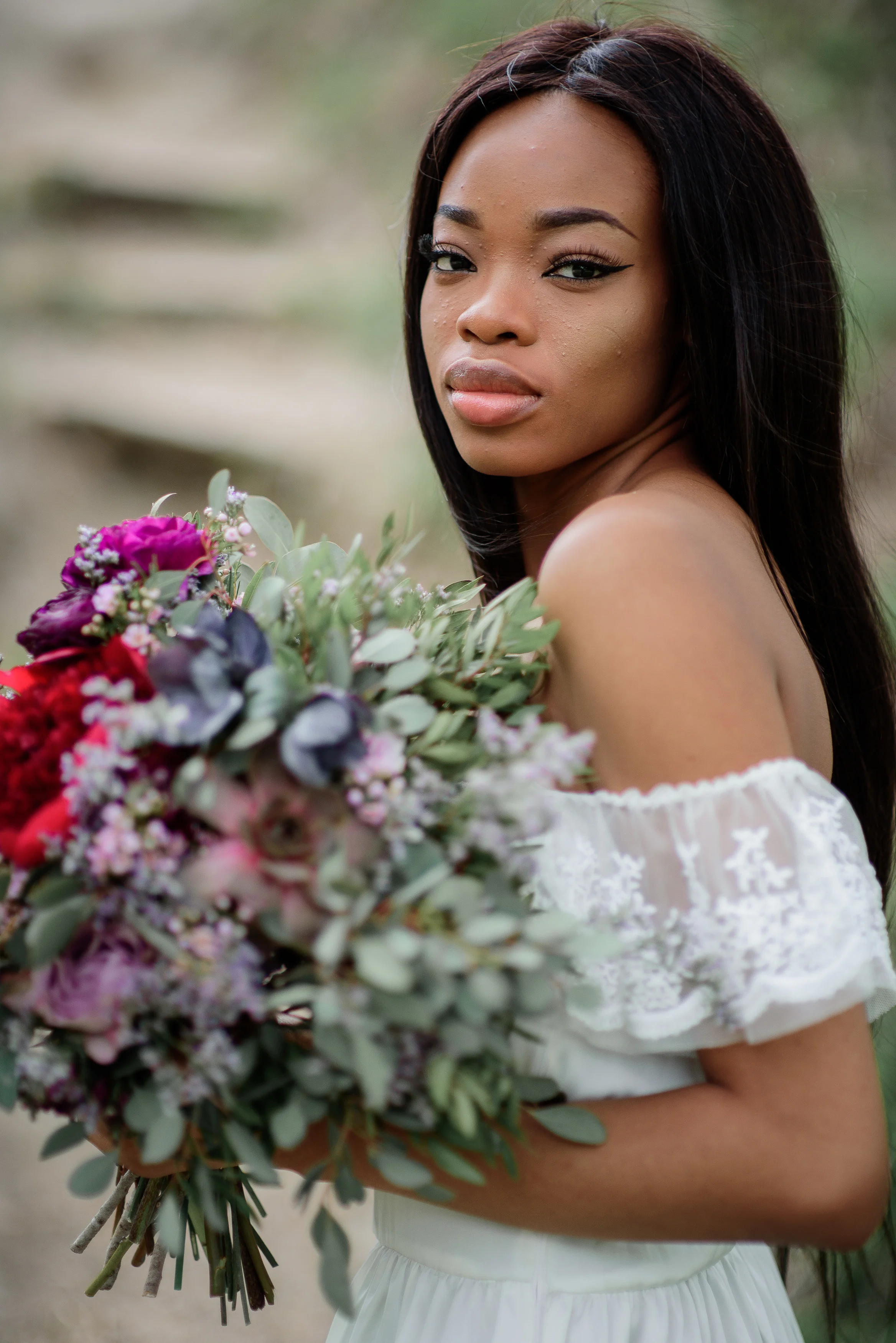 Bride with dark skin holds rich red bouquet in her tender arms