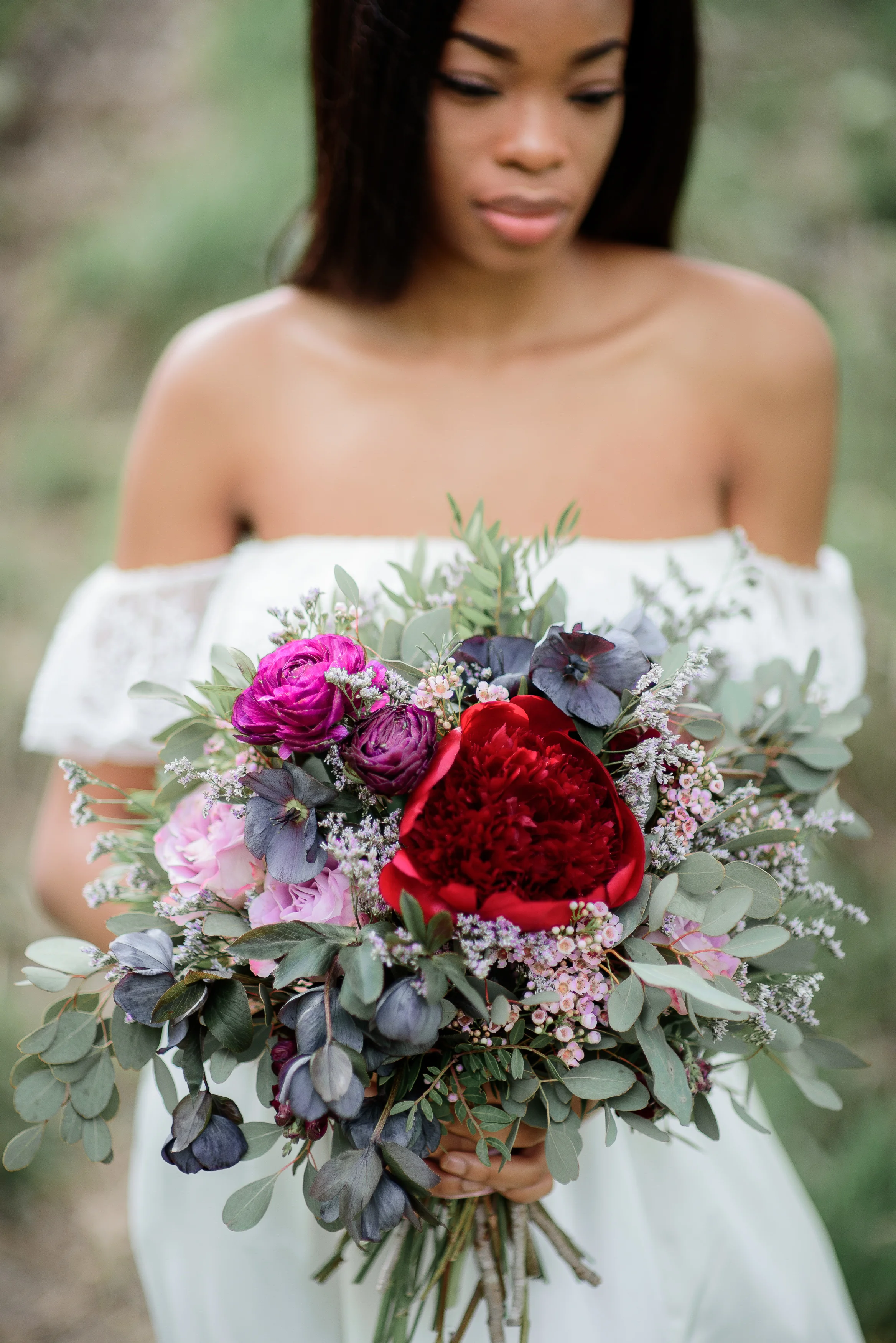 Bride with dark skin holds rich red bouquet in her tender arms