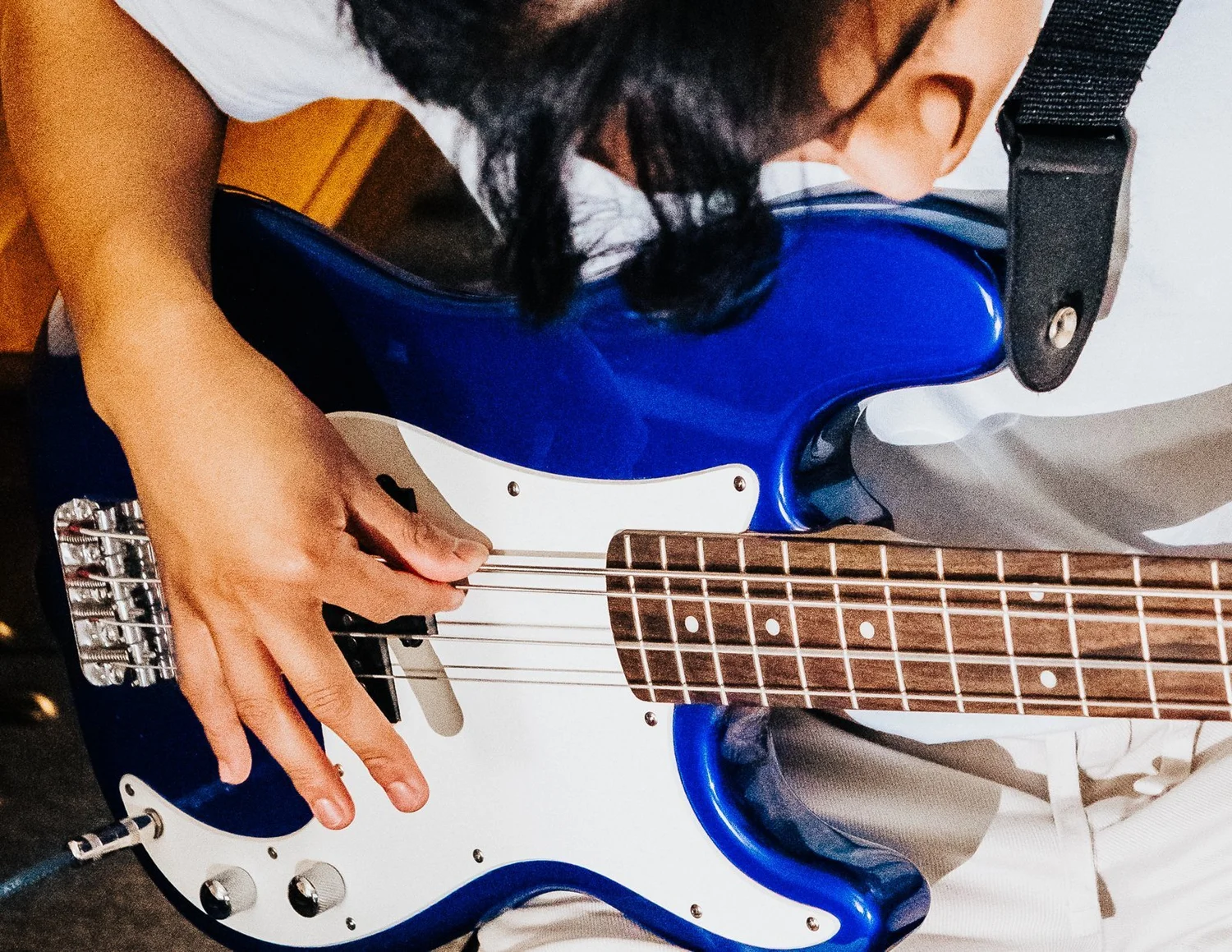 Gritty close-up of a Heart Beats student leaning over a blue electric bass