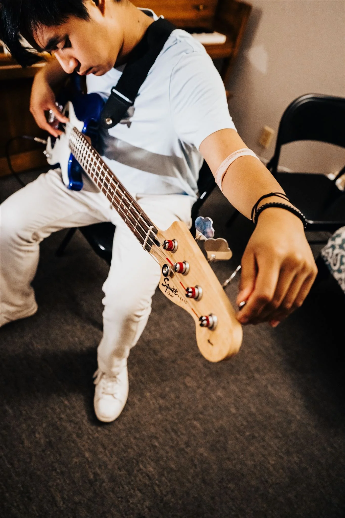 A Heart Beats student leaning over his electric bass and adjusting a tuning peg