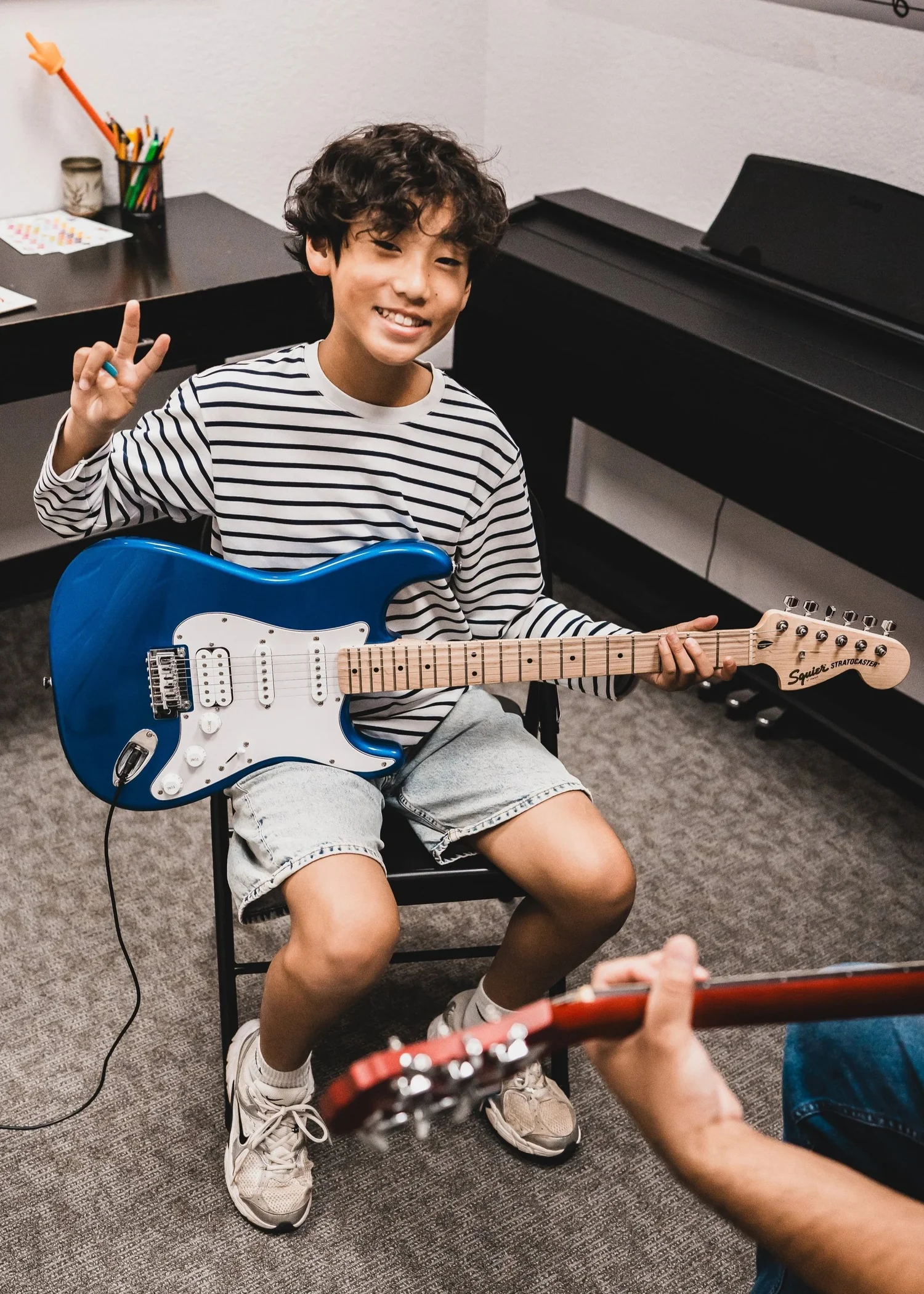 A smiling Heart Beats student gives a peace sign while holding his blue electric guitar