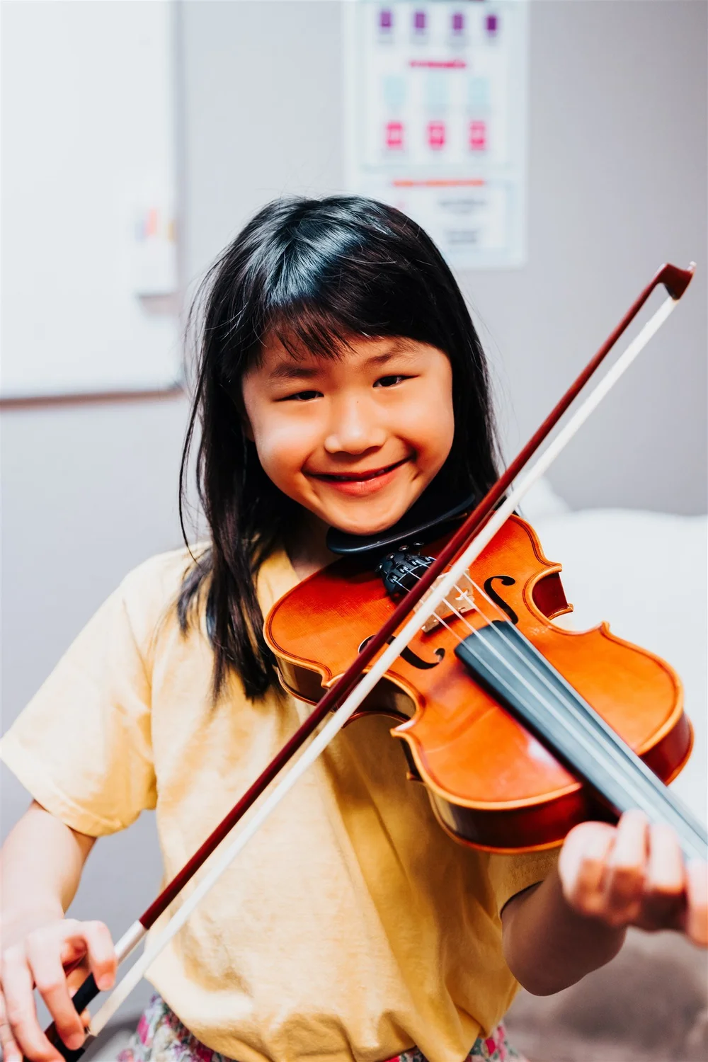 A smiling Heart Beats violin student in yellow playing her violin