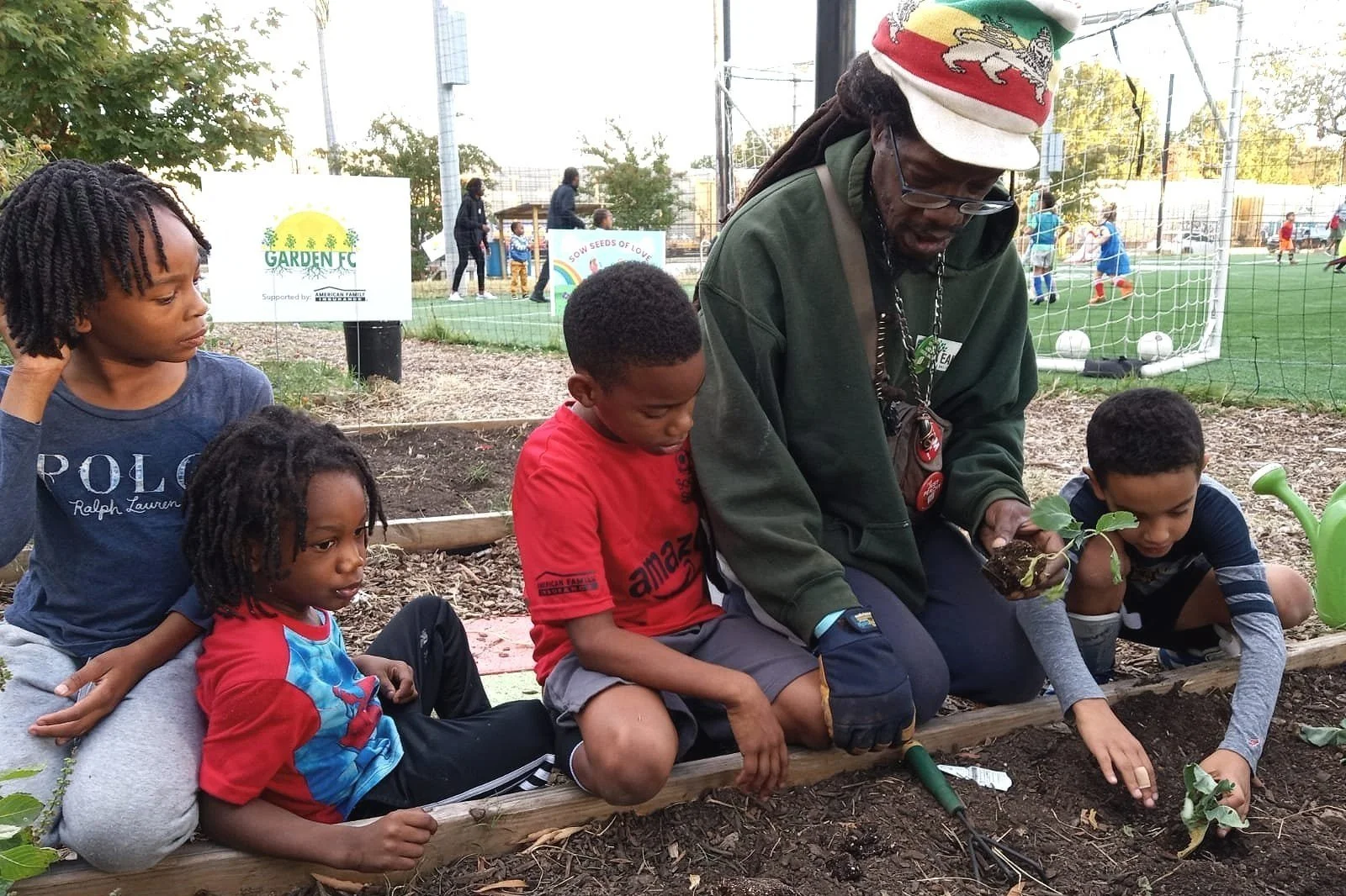 A group of children and an adult gardening near a soccer field.