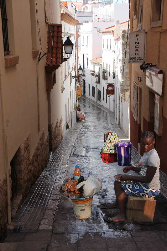 A Trader From Marina, Lagos Selling Her Wares In A Side Street In Sitges, Spain.