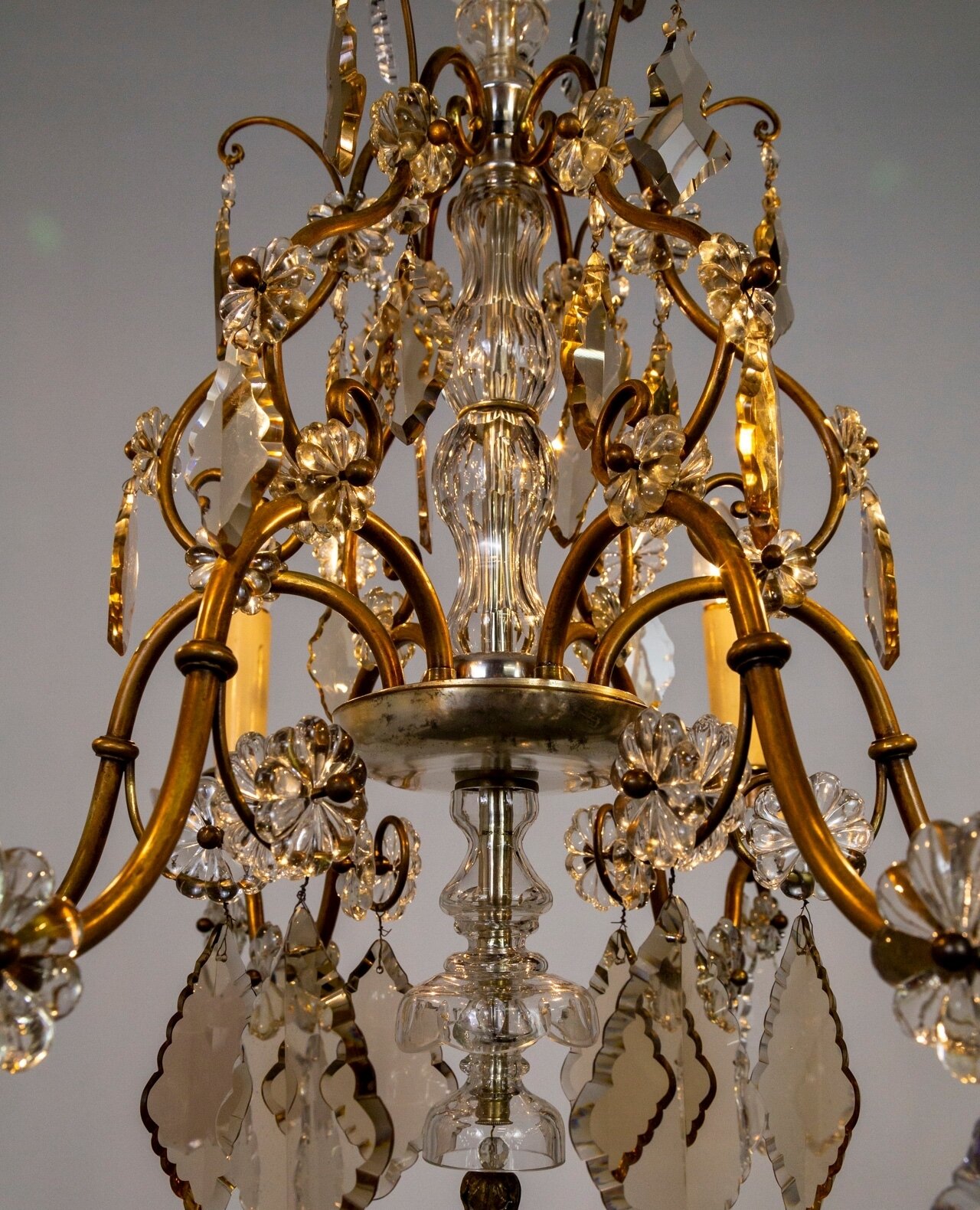 A magical, curling-armed, brass, candlestick-style chandelier. The large, finely cut, pendeloque, and scalloped diamond crystals are clear and smoke rose and amber. The brass arms are accented with rosette crystals and a silver-gilt dish body with cr