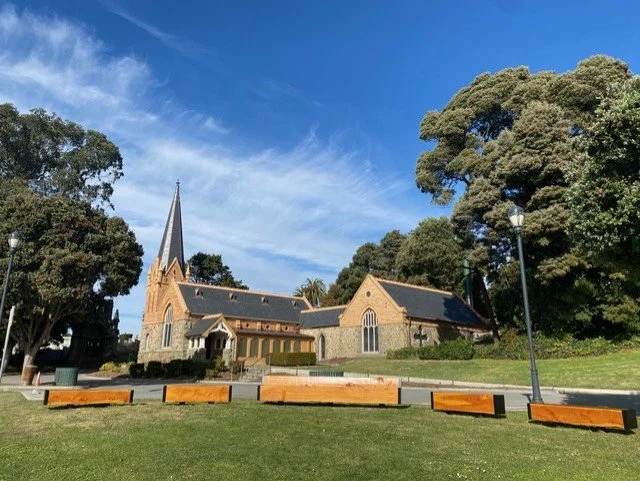 A church with a tall steeple surrounded by large trees and a grassy area, under a bright blue sky with few clouds.