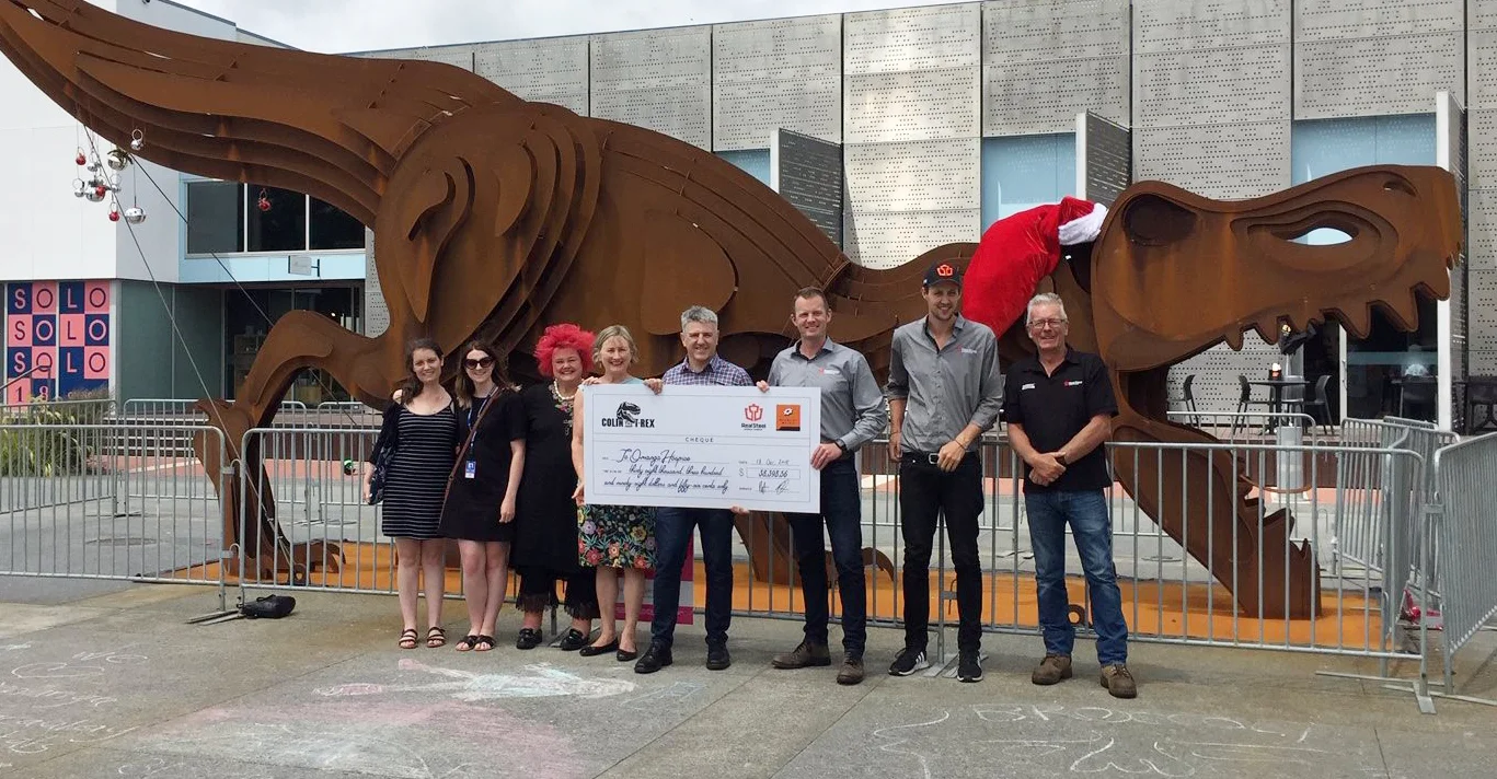 Representatives from Te Omanga Hospice, Macaulay Metals and Real Steel holding the cheque in front of Colin the T-Rex