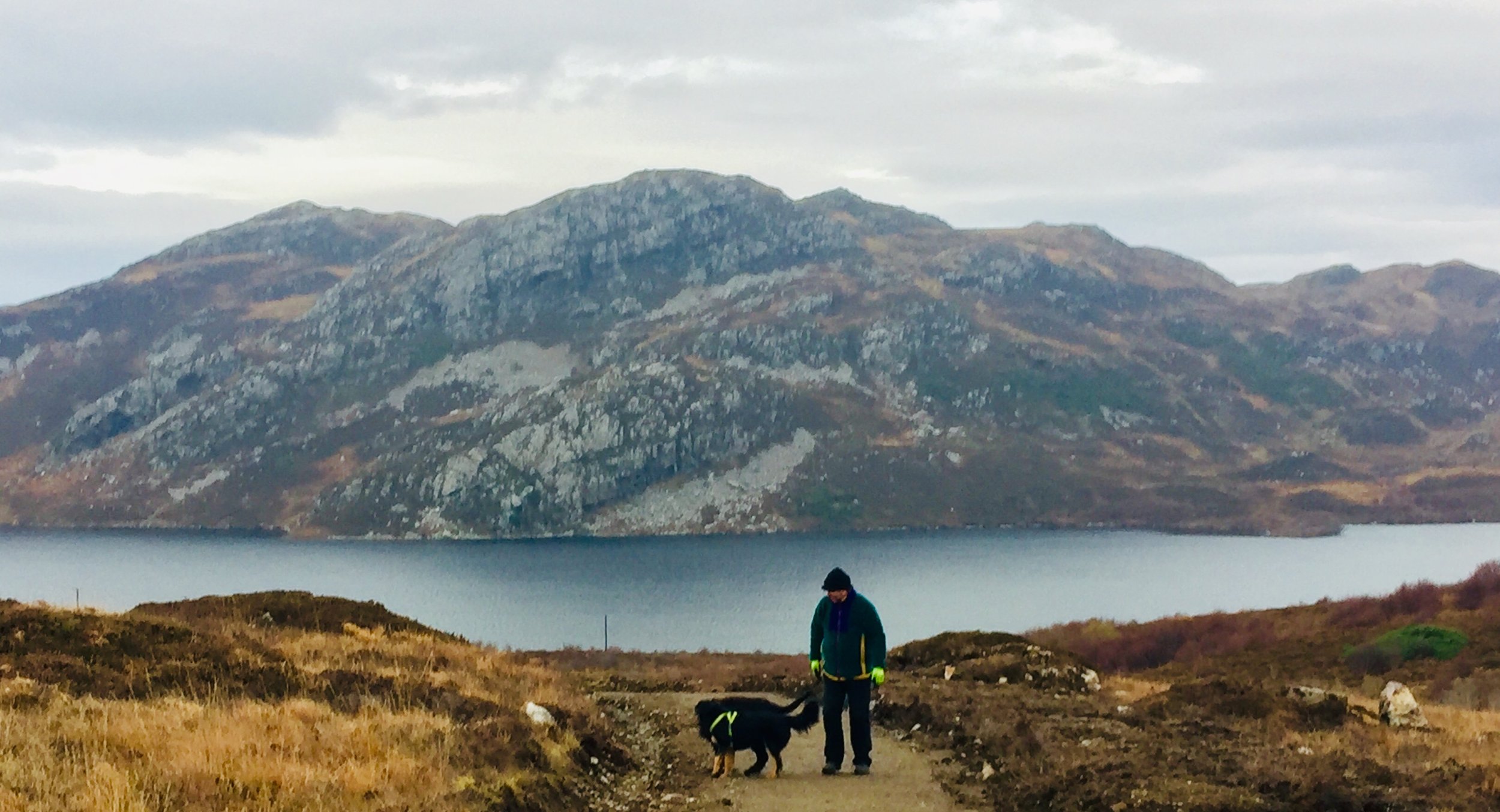Landscape photo of NW Sutherland landscape between Badcall and Scourie , dog walker with Black and Tan English Shepherd fog, hills rising sharply from loch