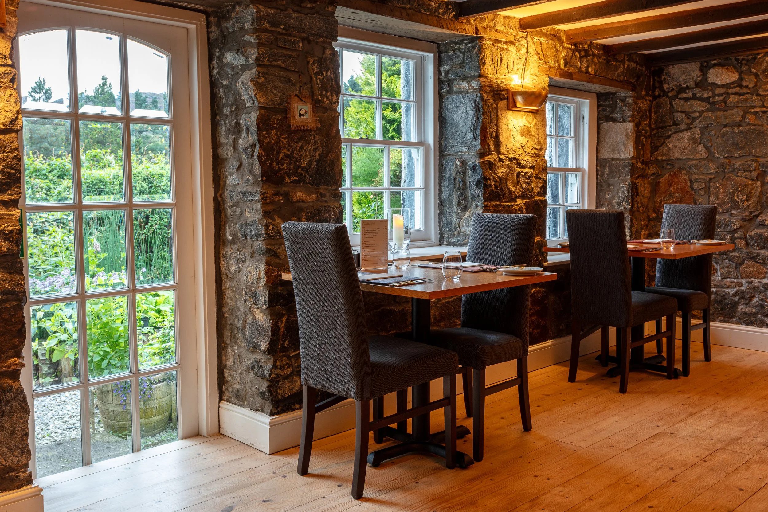 The Glebe Kitchen dining room at Eddrachilles Hotel with stone walls, wooden tables and views to the garden.