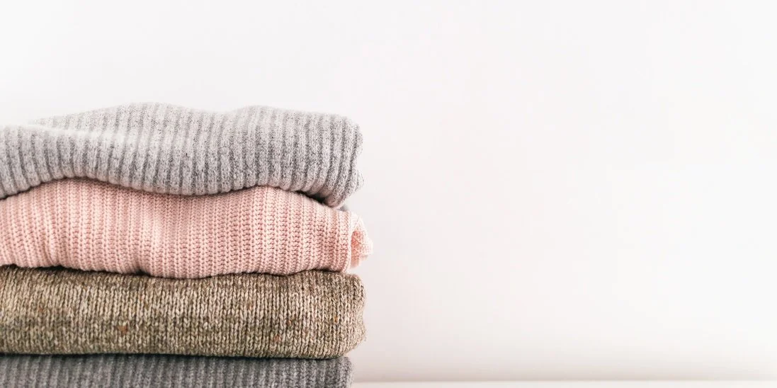 A stack of four folded sweaters in different colors arranged on top of one another against a white background.