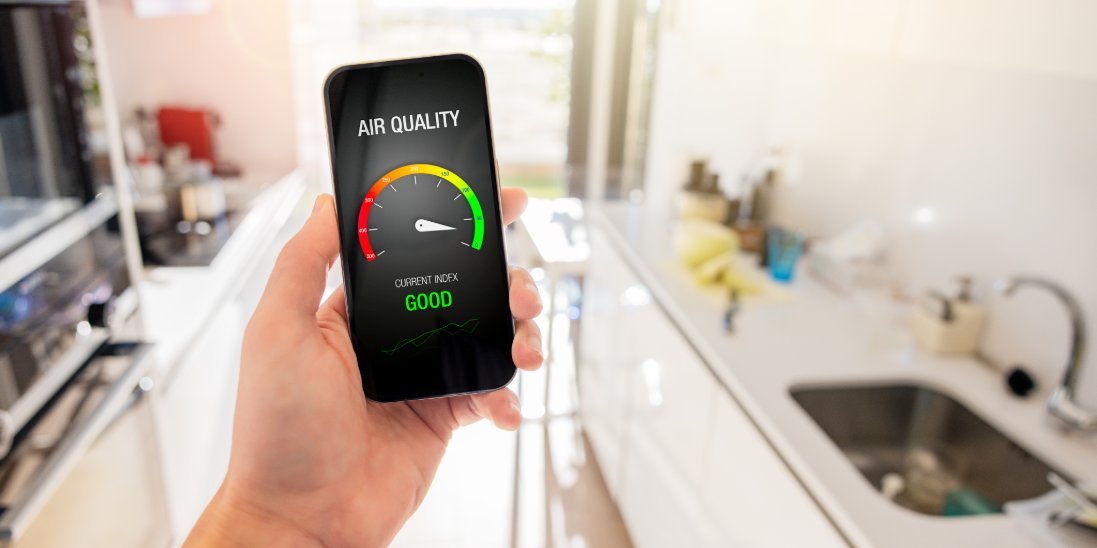 A person is standing in a kitchen as they hold up their phone. On the phone, it’s displaying an air quality gauge.