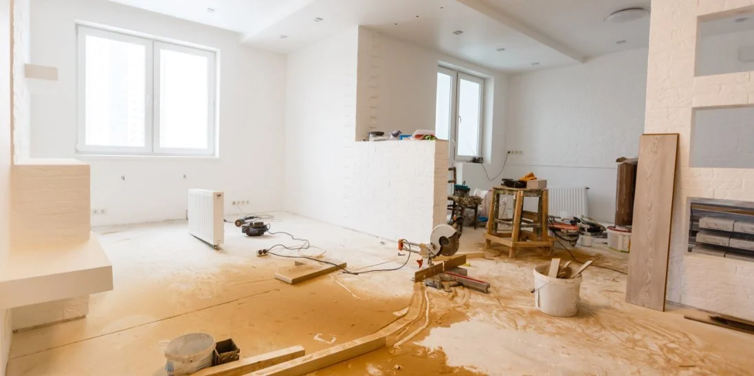 A residential home is under construction. The floor is unfinished and there are no curtains on the windows.