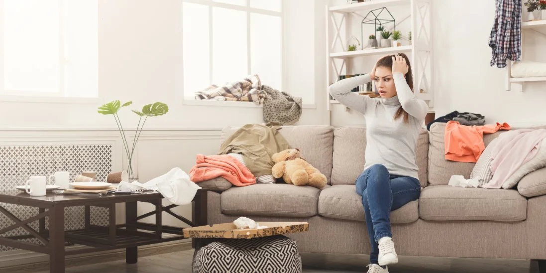 A young mom sits on her family sofa in the living room as she appears frazzled by the clutter around the space.