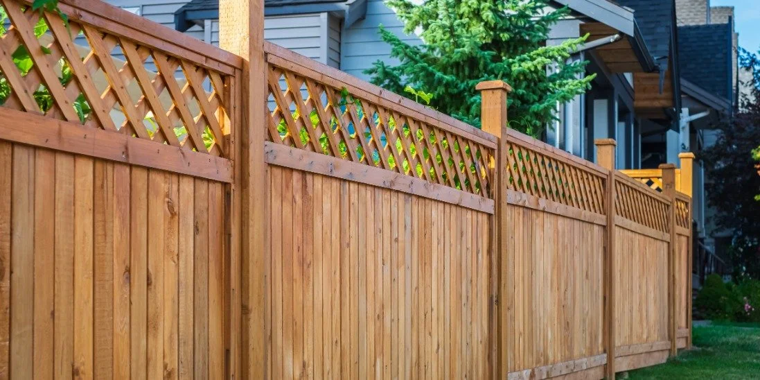 Wooden privacy fence with lattice panels and tall posts enclosing a grassy backyard beside a gray house.