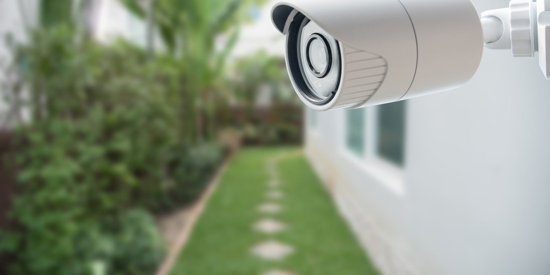 A security camera mounted on a home's exterior gutter guard. The path below the camera has a walkway in the grass.
