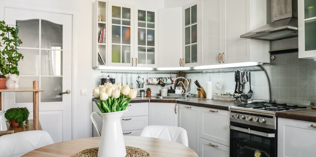 A small kitchen with white interior and brand new glass cabinets with a bouquet of tulips on the dining table.