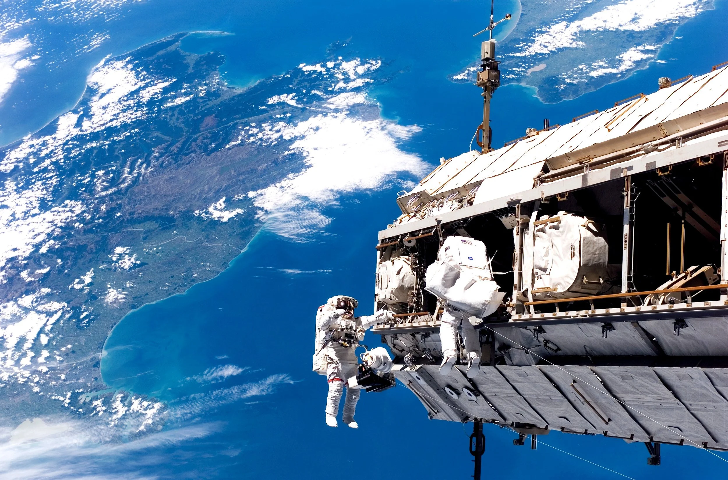  U.S. astronaut Robert Curbeam (left) and Swedish Astronaut Christer Fuglesang rewire the Station's electrical system in December 2006. The land mass below is New Zealand. Photo credit: NASA.
