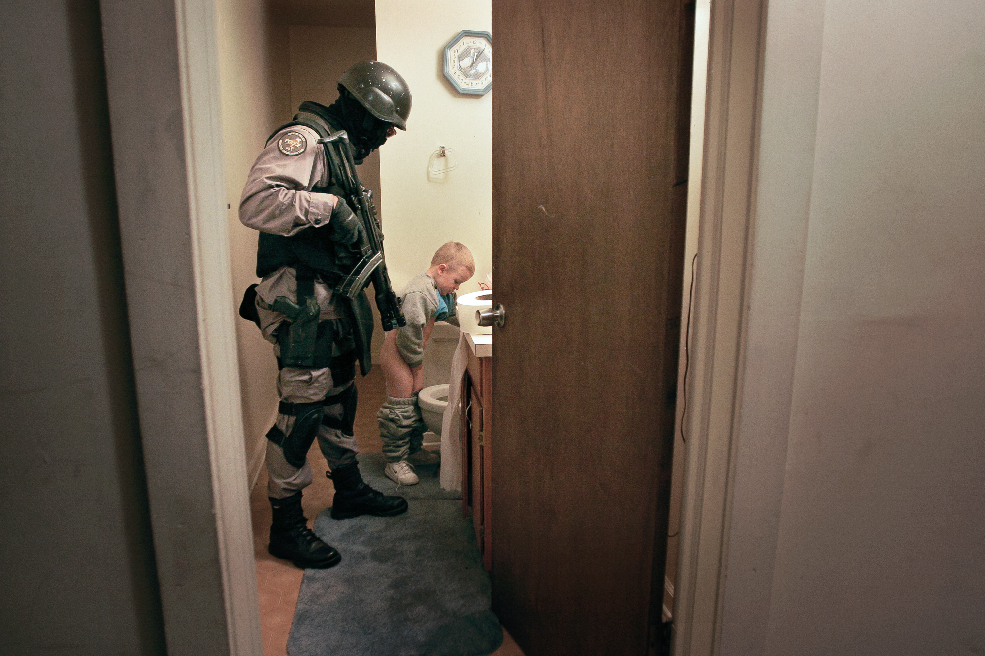  After a drug raid in 2005, a member of the Durham Police Department Selective Enforcement Team escorts a child to the bathroom. His mother was temporarily detained during the search of the home and couldn’t tend to him. Through raids, officers hope 