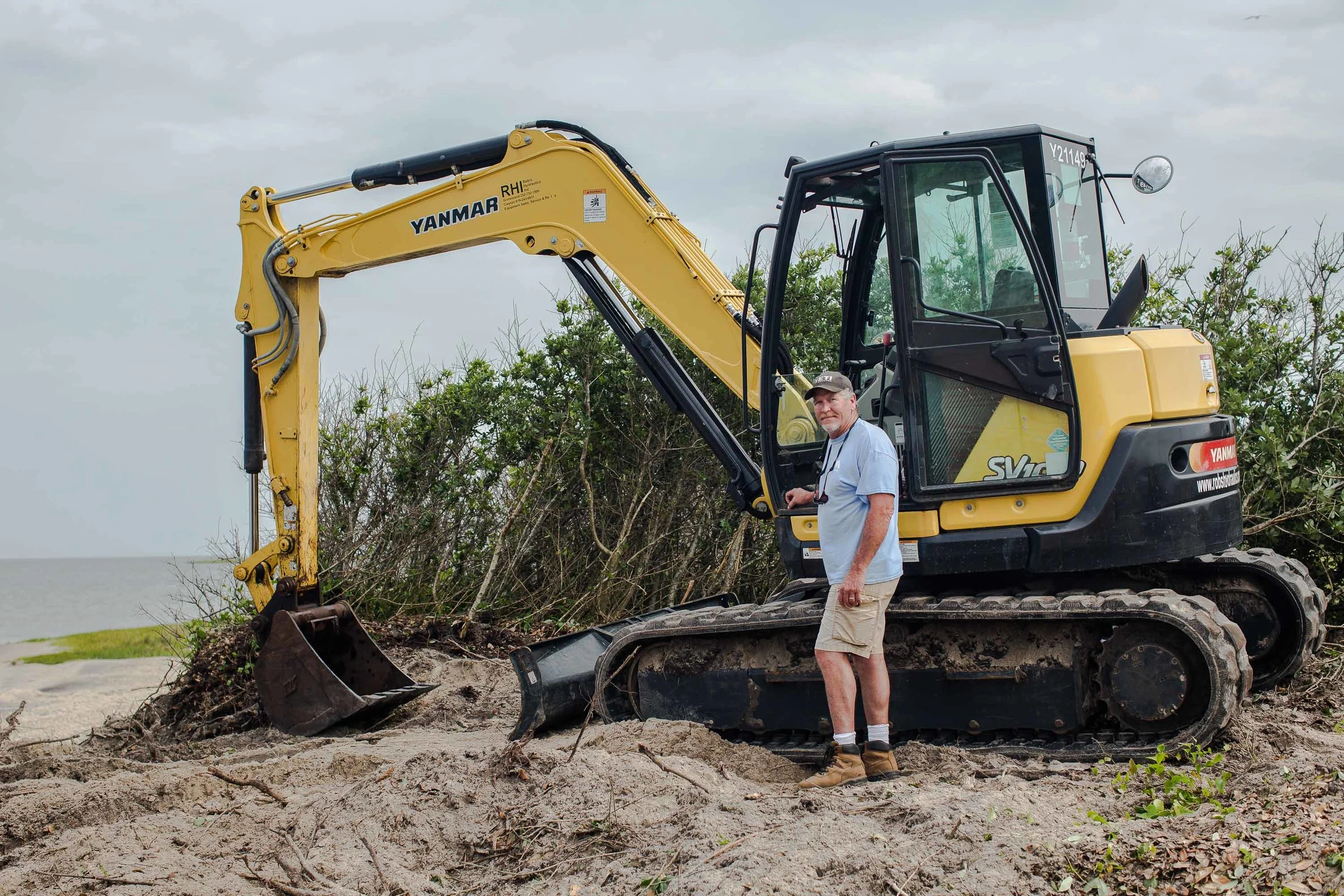 David “Cowboy” Ambrose poses with his backhoe. His marine construction company is building a bulkhead that will slow erosion between the sound and the Salvo Community Cemetery. Decades ago, he fell in love with the Outer Banks and never left. “People call me cowboy because wherever I take my boots off is my home,” he says. May 2018.