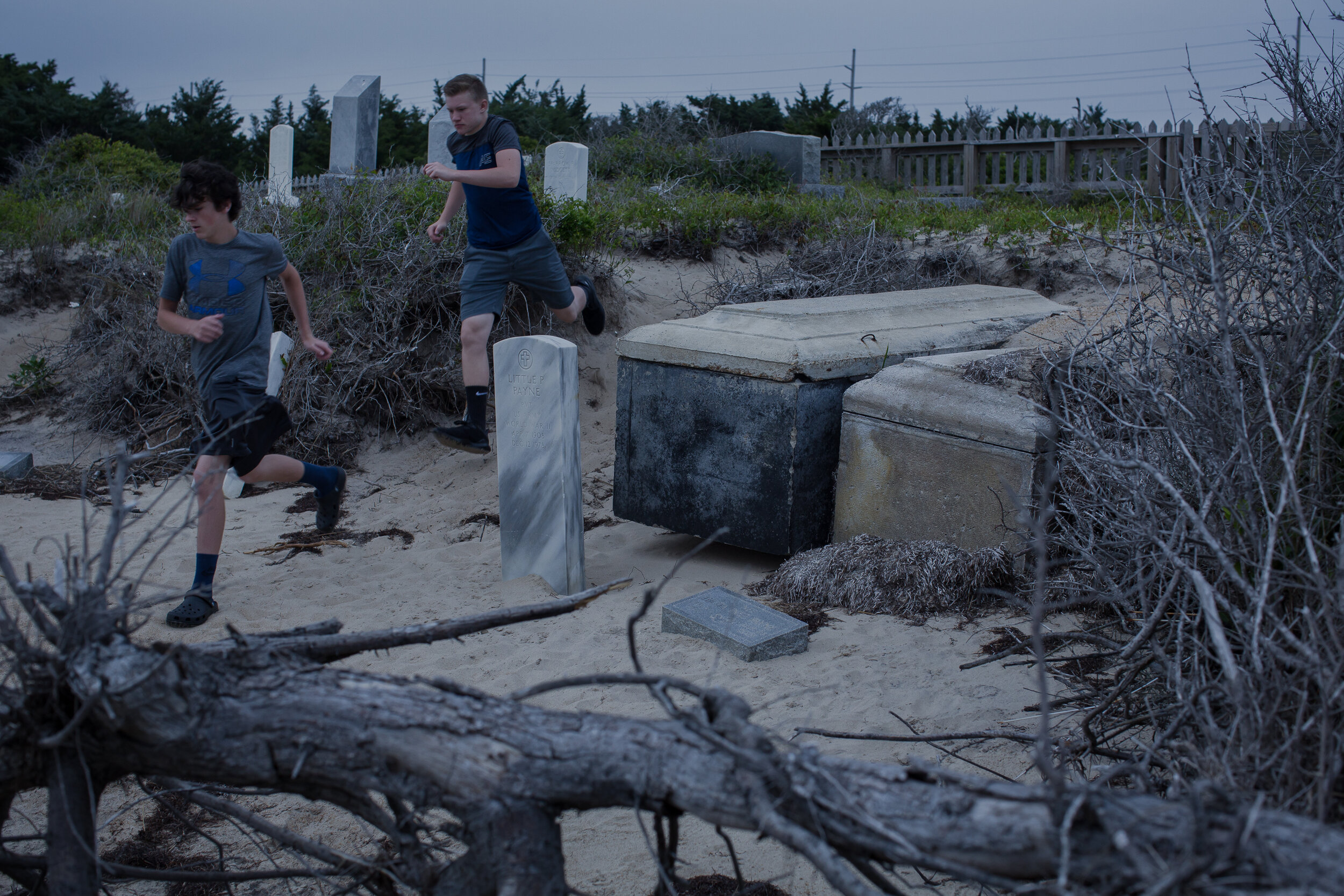  In May 2017, tourists ran past the graves of Little Pharaoh Payne, a WWII veteran, and his wife, Hilda, which have been exhumed by storm surge. Threatened by erosion and sea level rise, the cemetery is also vulnerable to foot traffic, which wears aw