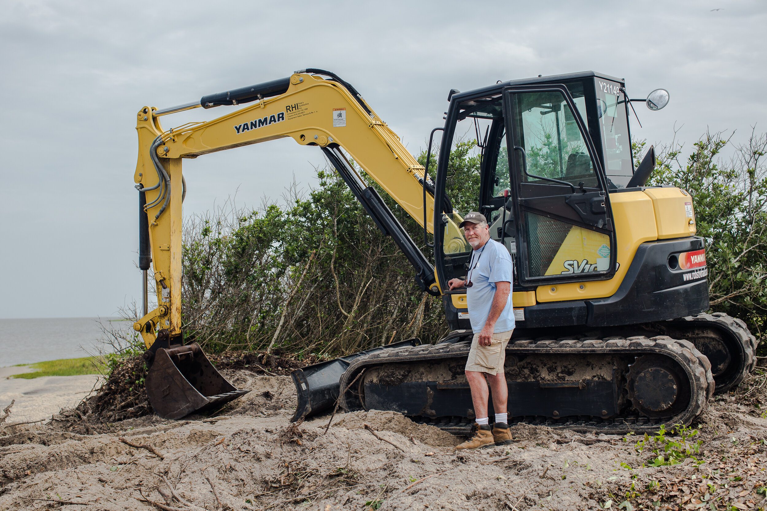  David “Cowboy” Ambrose poses with his backhoe. His marine construction company is building a bulkhead that will slow erosion between the sound and the Salvo Community Cemetery. Decades ago, he fell in love with the Outer Banks and never left. “Peopl