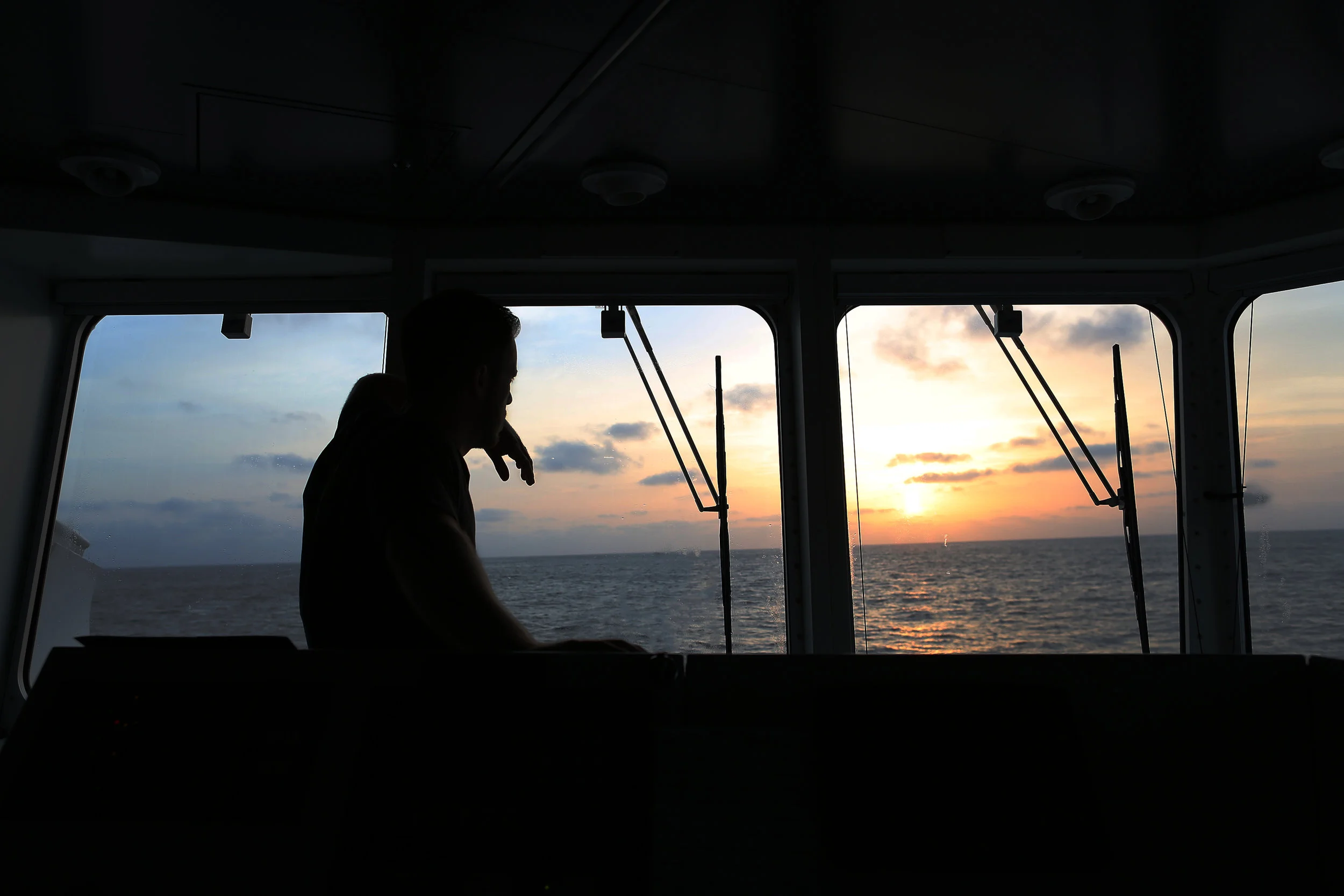 Chief Officer Jason Garwood watches the sunrise from the bridge of R/V Falkor .
