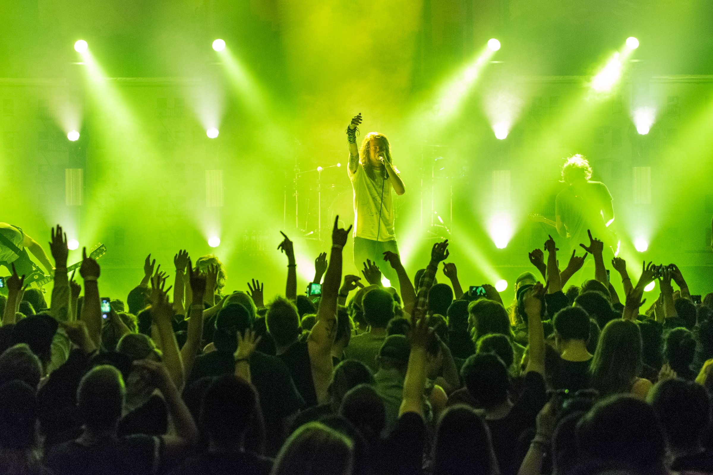 A concert with green stage lighting, a singer holding a microphone, and an audience with raised hands.