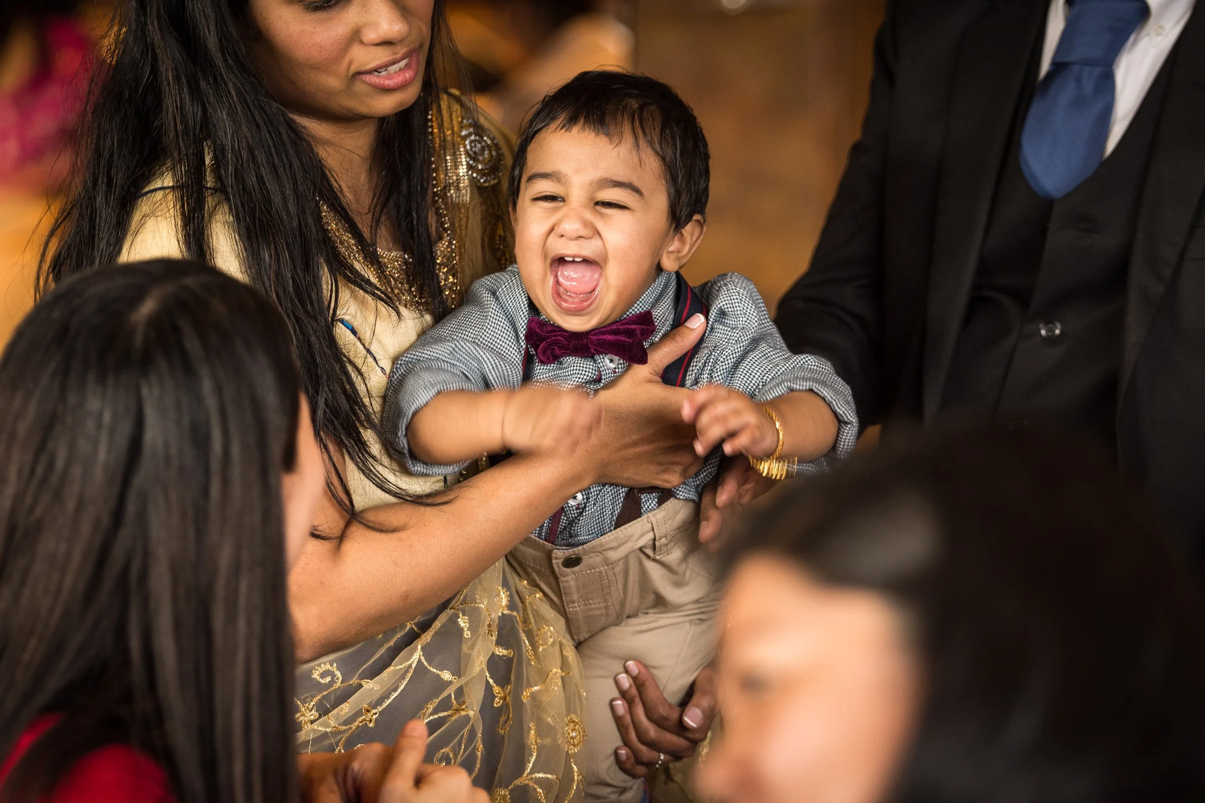 A group of people, including a woman and a young boy, are gathered closely together at an event. The boy is crying with his mouth open, and the woman is holding him gently, appearing concerned or comforting. The scene appears emotional, and the backg
