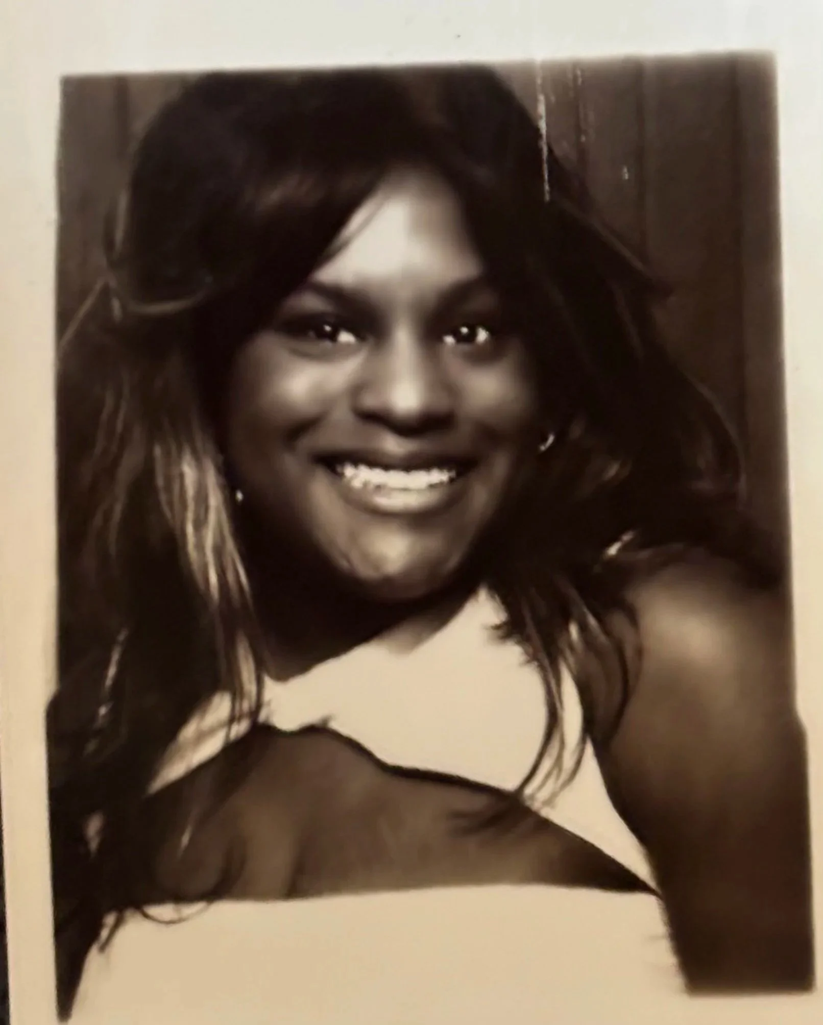 A woman with a photo booth, glasses resting on her head, smiling broadly, making a peace sign near her eye, and wearing a ring and earrings.