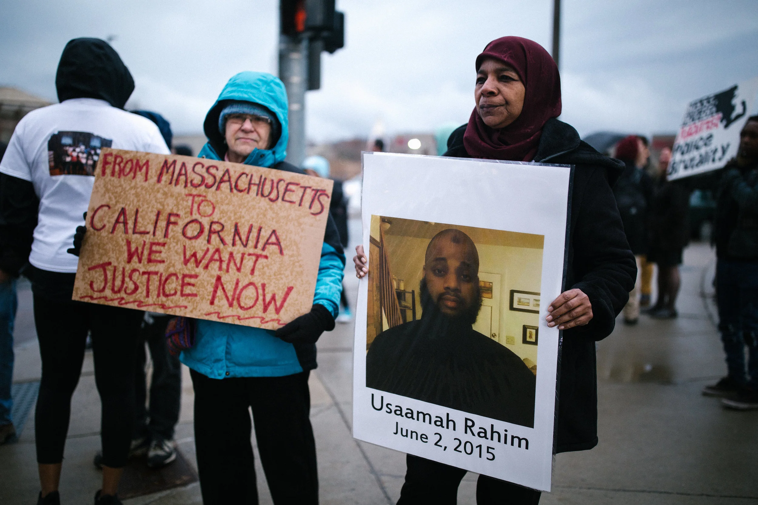 Photo description: Rahima Rahim, pictured on the right, holds a sign with the picture of her son Usaamah Rahim and the date June 2, 2015, when he was killed by Boston police and FBI in Roslindale. To the left, an unidentified protester holds a sign that says ‘From Massachusetts to California We Want Justice Now.’ (Credit: Emily Goldhammer)