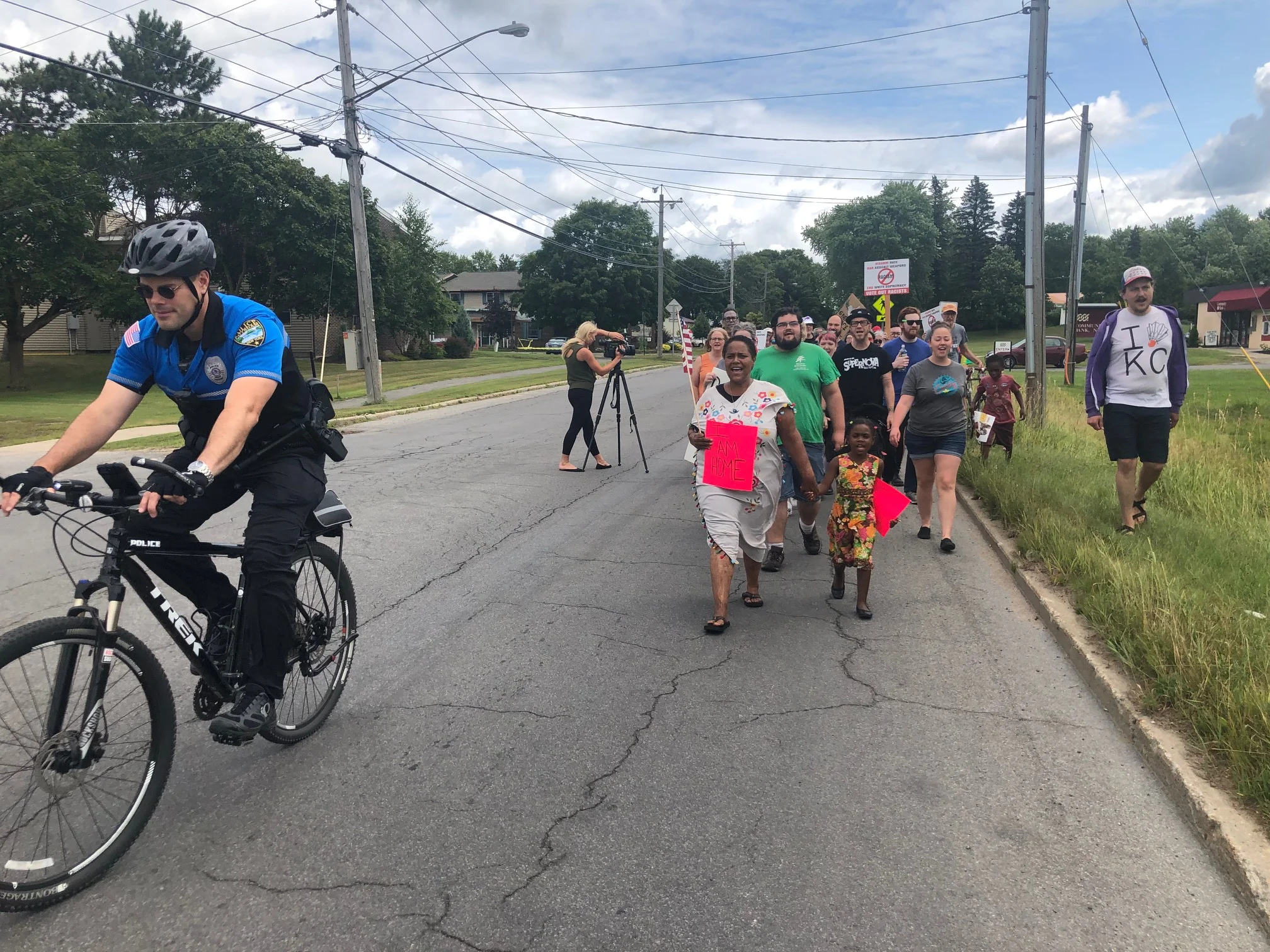 A member of the Potsdam police accompanies demonstrators as they make their way down May Street toward Market Street.