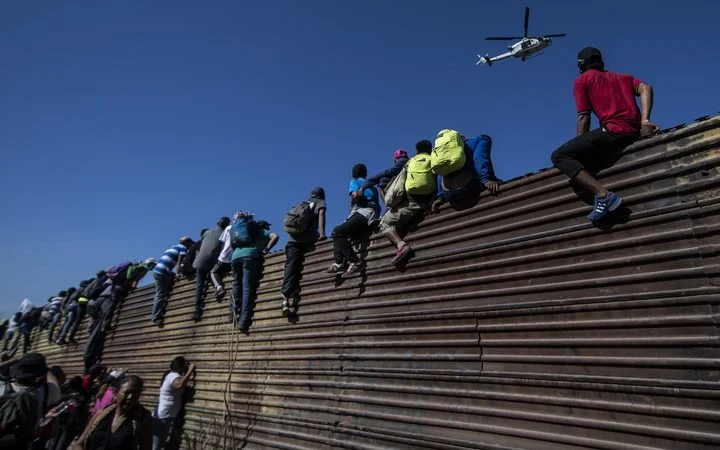 Migrants climb across walls and other barricades in an attempt to enter the US