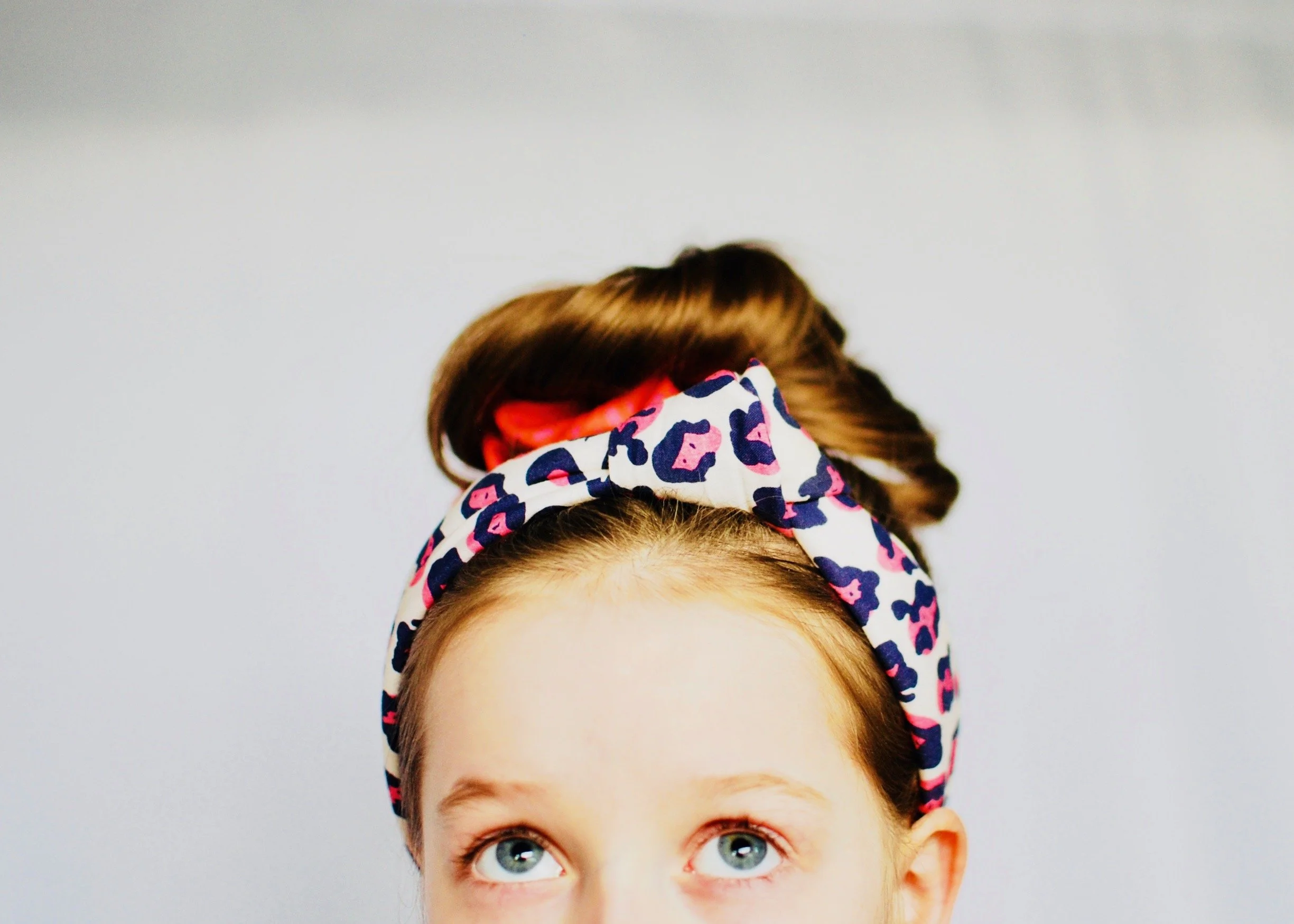 blue eyed young girl with her hair in a bun and a she is fierce lysa flower leopard print headband.jpg