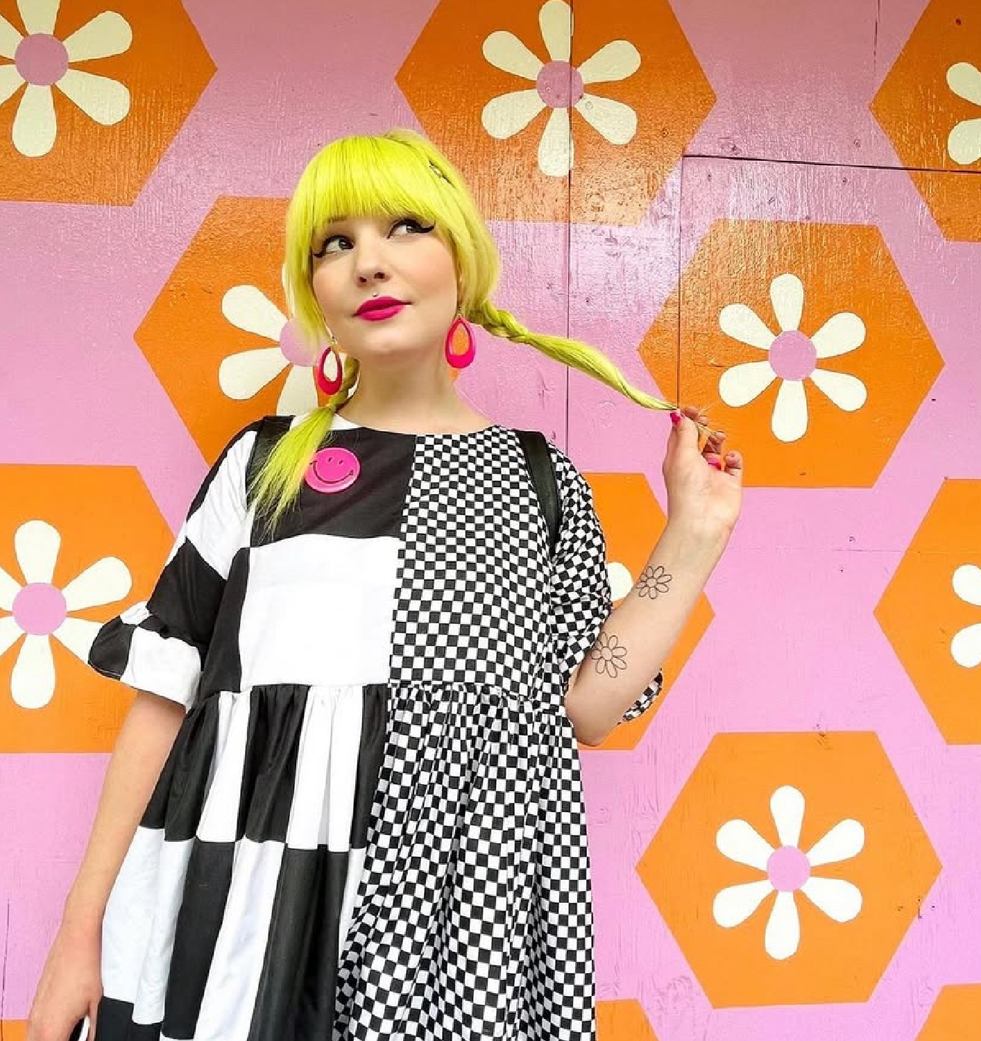 young woman with green yellow hair in braids wearing a black and white checkered dress in front of lysa flowers dresssew mural in vancouver.png