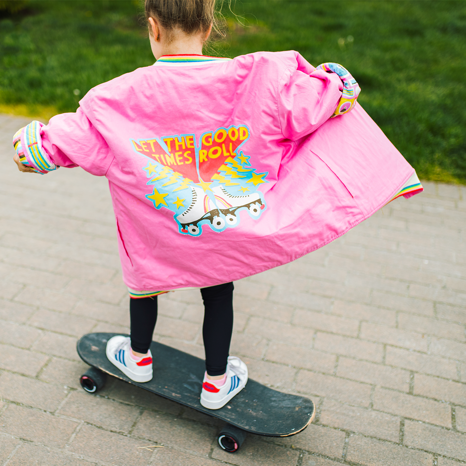 girl skate boarding wearing a pink let the good times roll jacket at a park.png