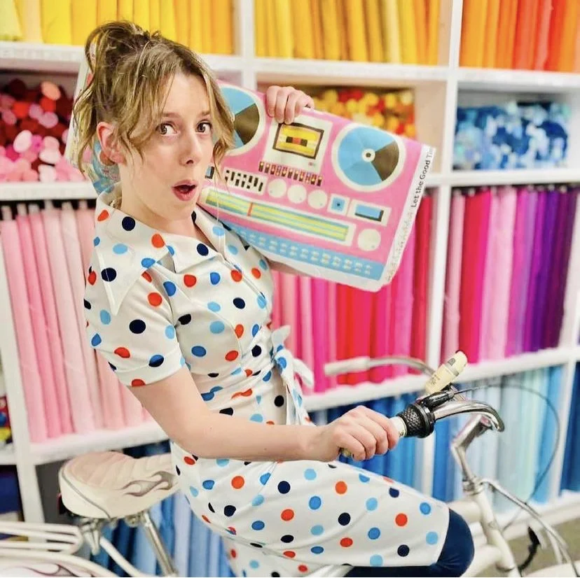 woman on bike with a bolt of lysa flower boombox fabric on her shoulder pretending its a real boomboc.jpg