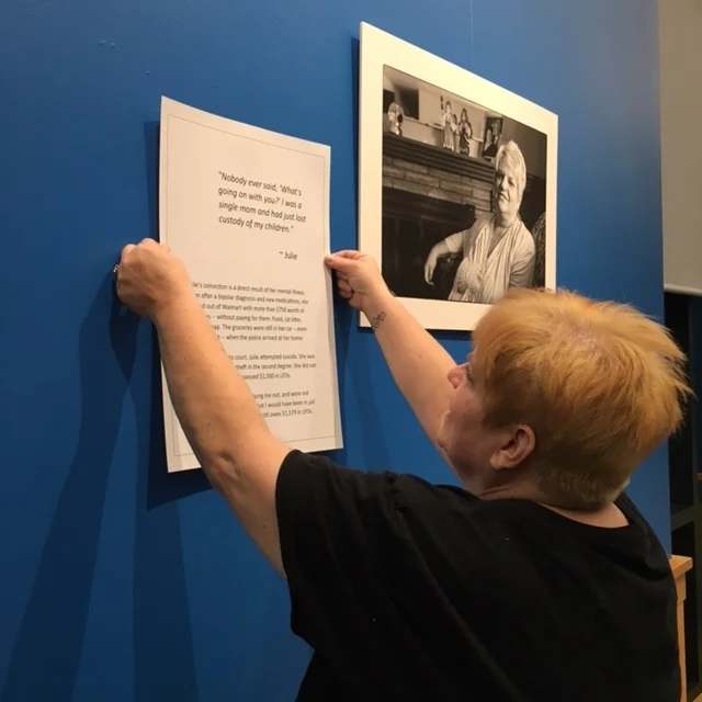   Living with Conviction  participant Julie Kelly helps hang her portrait and quote at the Spokane Public Library in January 2018. 