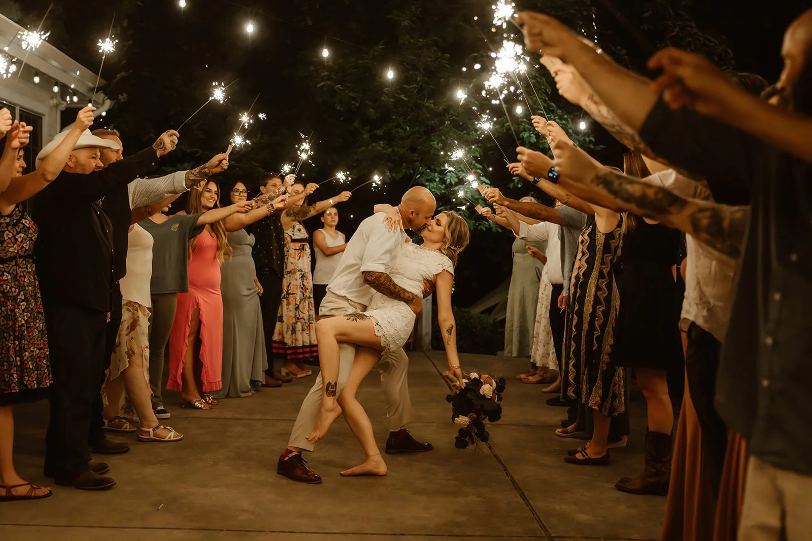 A couple dances closely amidst a circle of people holding sparklers during a celebration, likely at night.