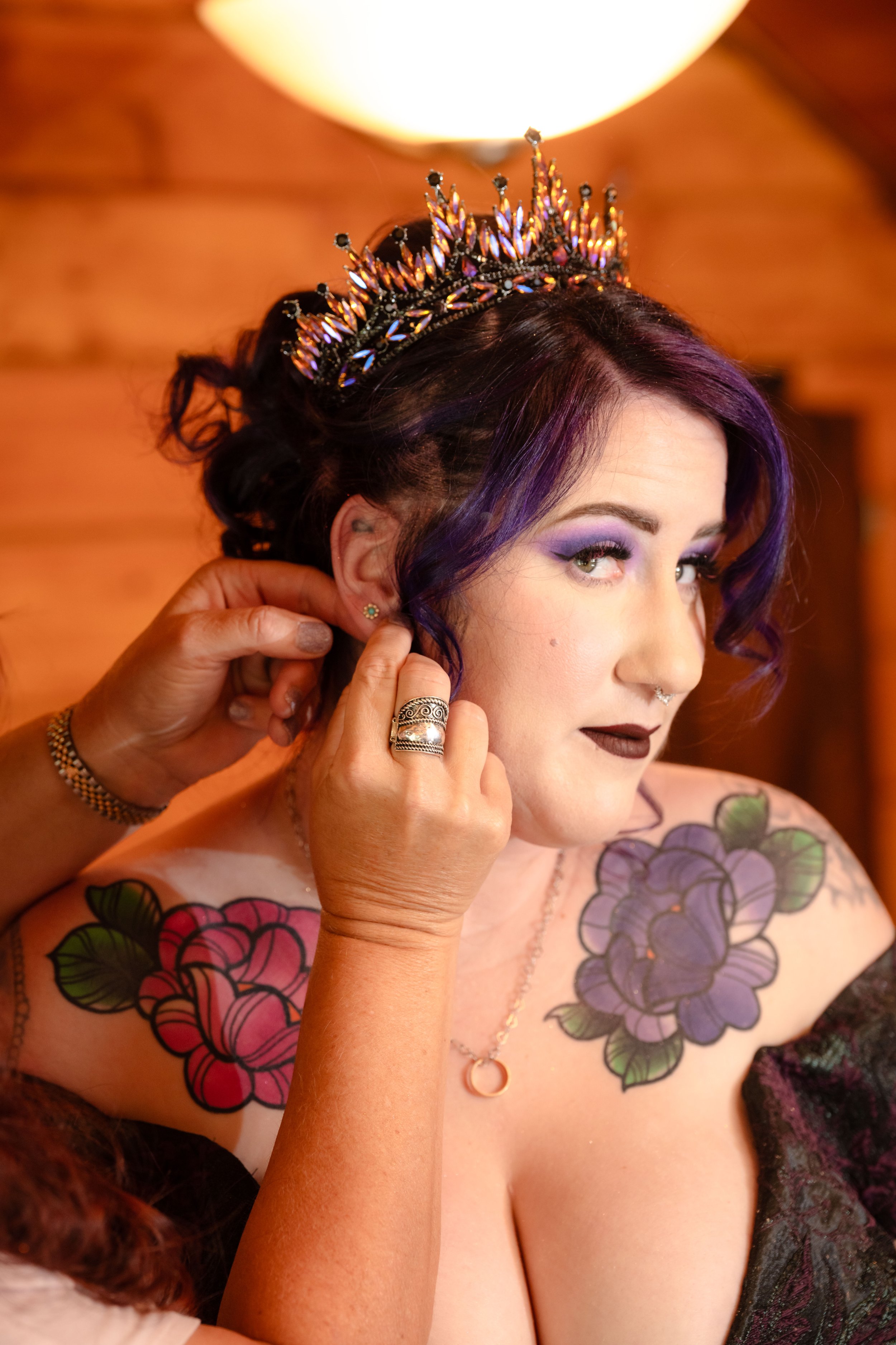 a gothic bride wearing purple bridal makeup is assisted with putting on her jewelry