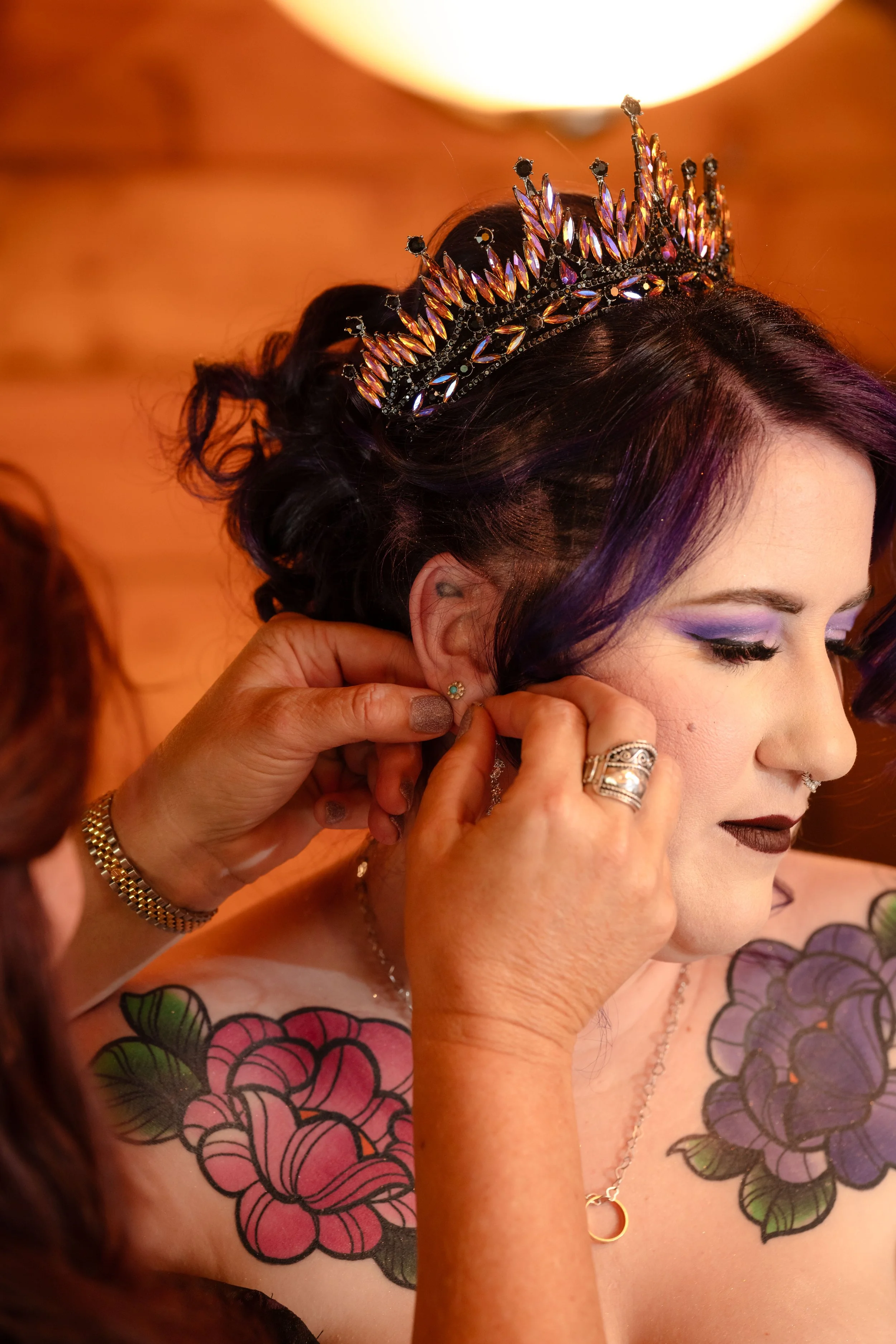 a gothic bride wearing purple bridal makeup is assisted with putting on her jewelry