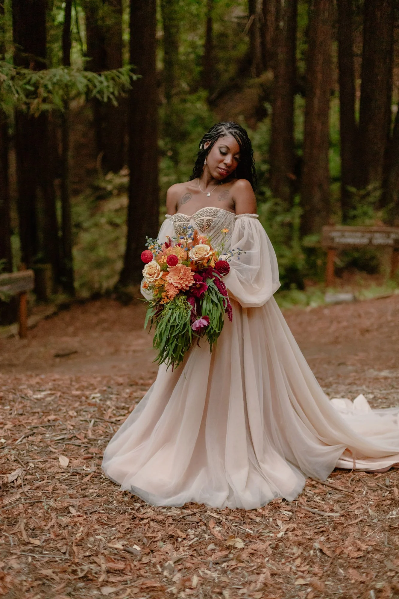 A bride in a strapless cream-colored wedding gown holding a colorful bouquet of flowers in a forest setting.