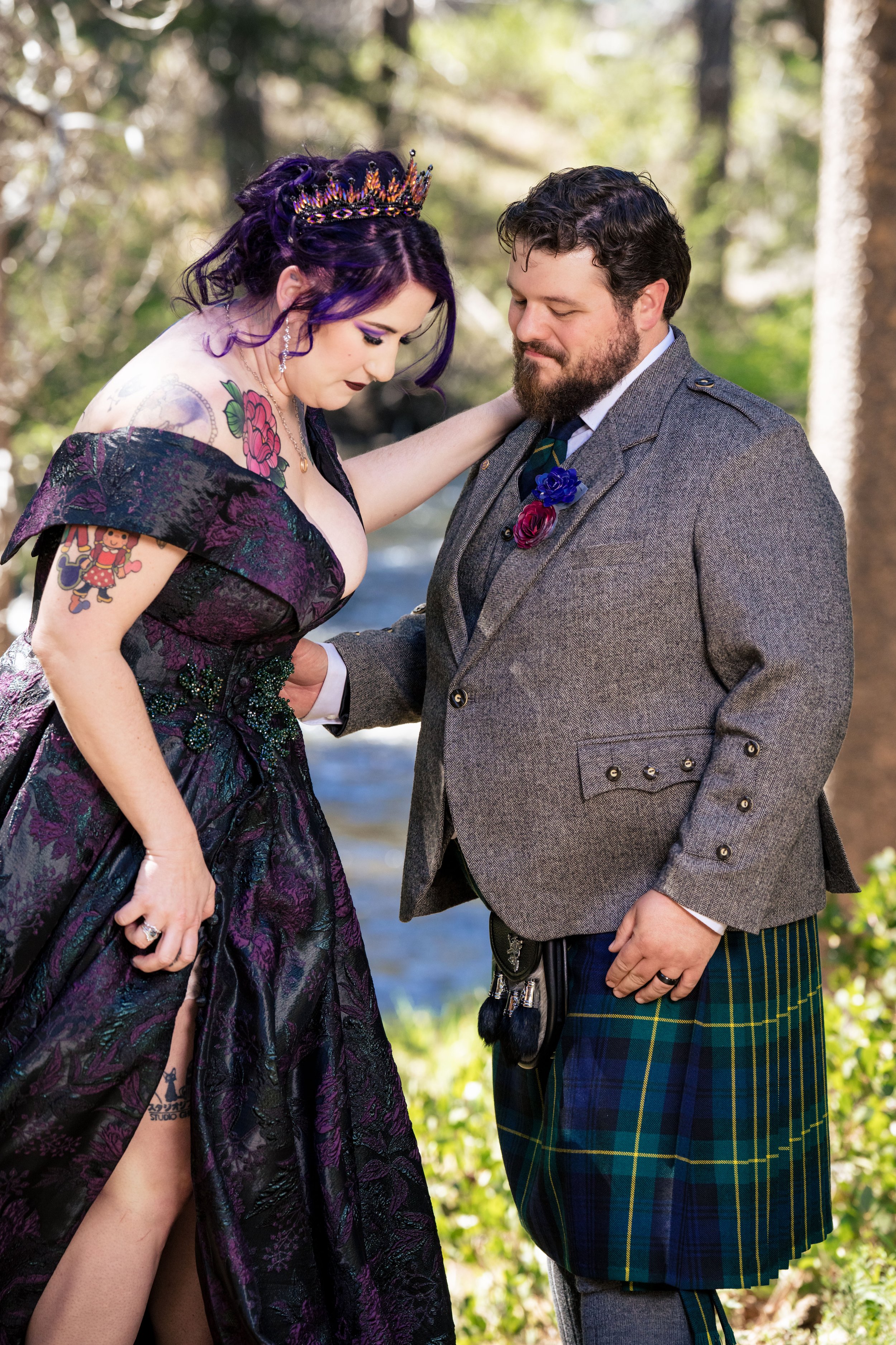 a gothic bride with tattoos wearing a black dress stands with her husband. she is wearing gothic glam makeup 