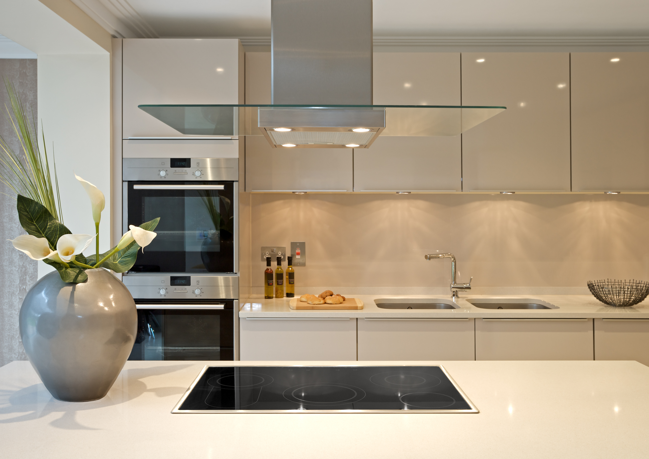 Modern kitchen with glossy cabinets, stainless steel appliances, induction cooktop, glass range hood, and stylish countertop décor, highlighting professional home renovation and interior design transformation.