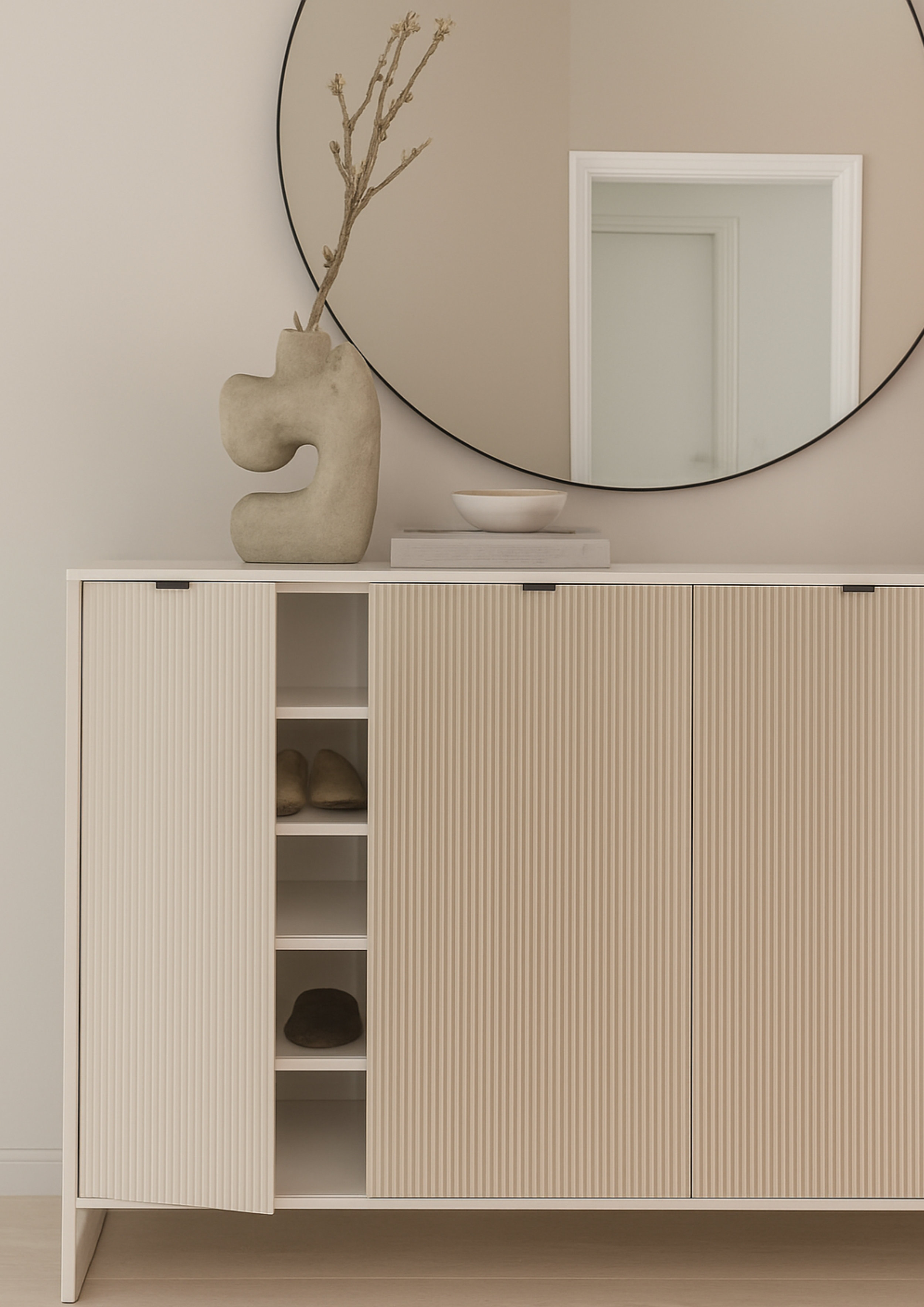 Entryway console with fluted cabinet doors, round mirror, and sculptural décor in neutral tones, showcasing modern minimalist home interior design.